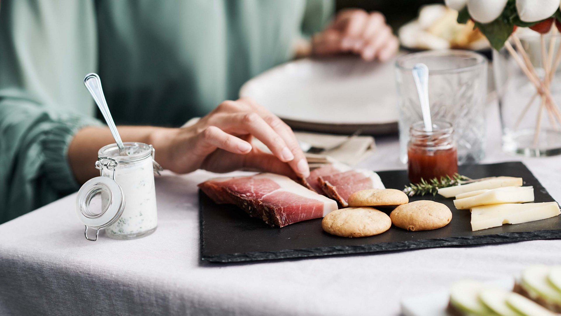 Persona prende prosciutto da vassoio con formaggi, biscotti e salse