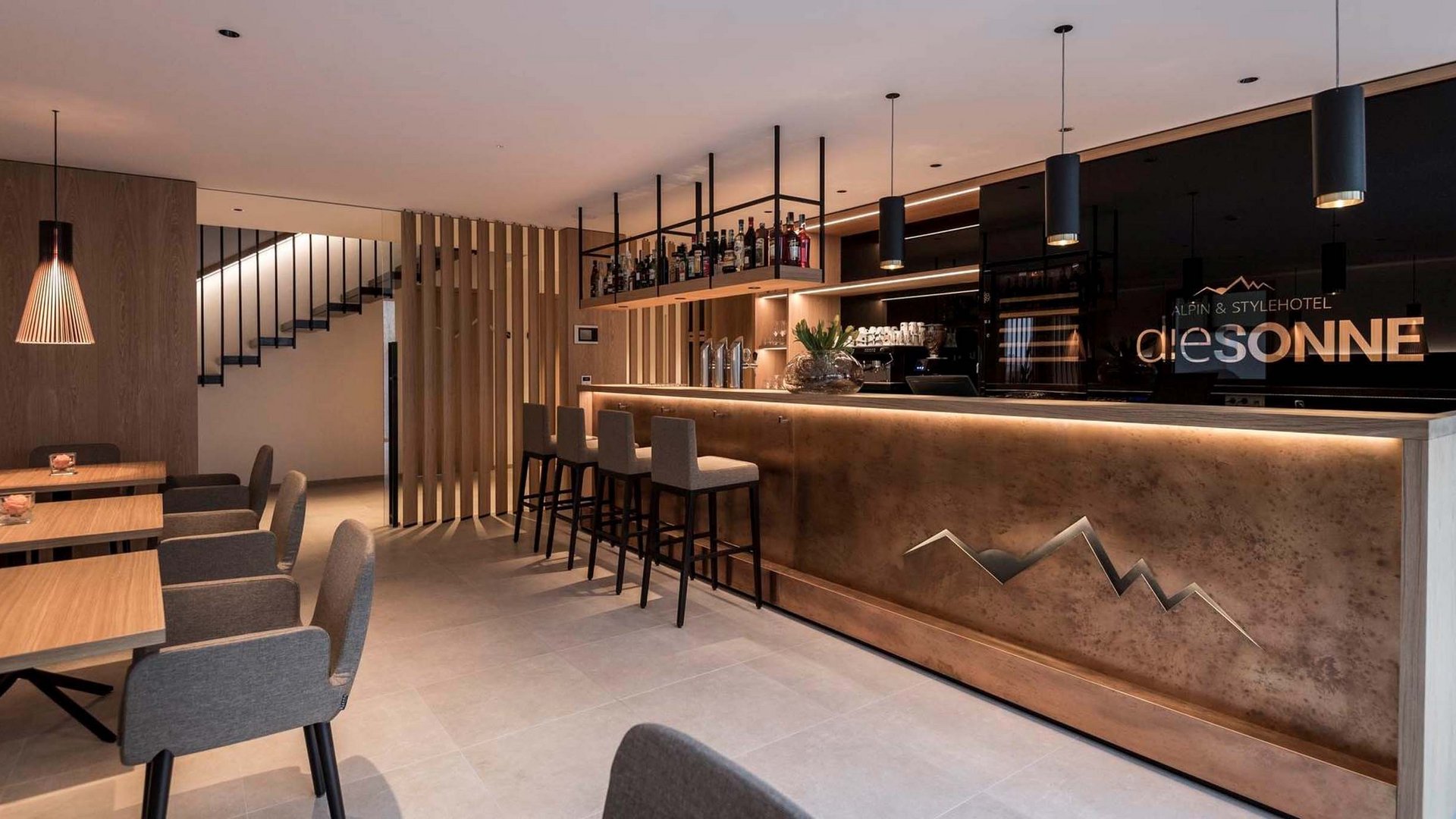 Area bar moderna con bancone e sedie nell'Alpin & Stylehotel