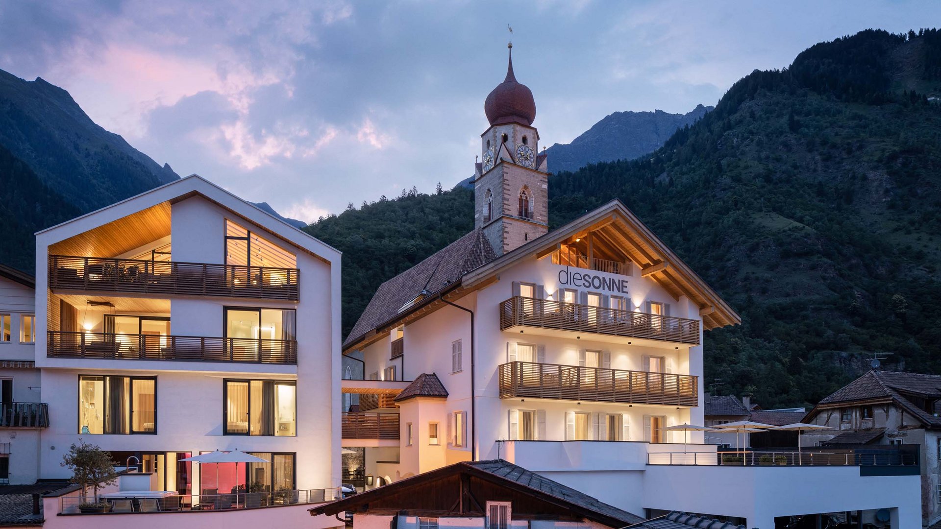 Edificio moderno accanto a una chiesa tra le montagne al crepuscolo