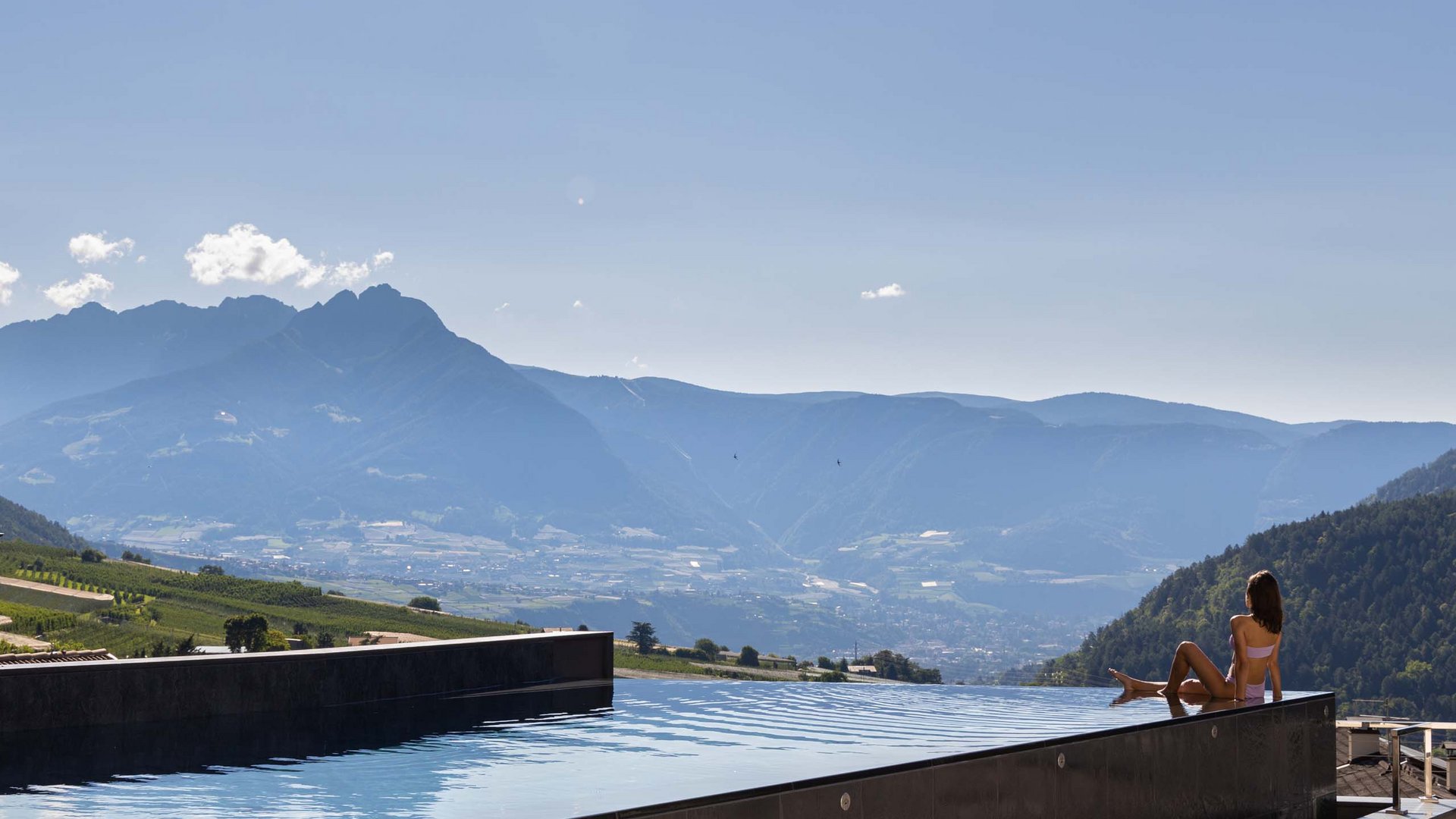 Frau entspannt am Infinity-Pool mit Blick auf Berge und Tal
