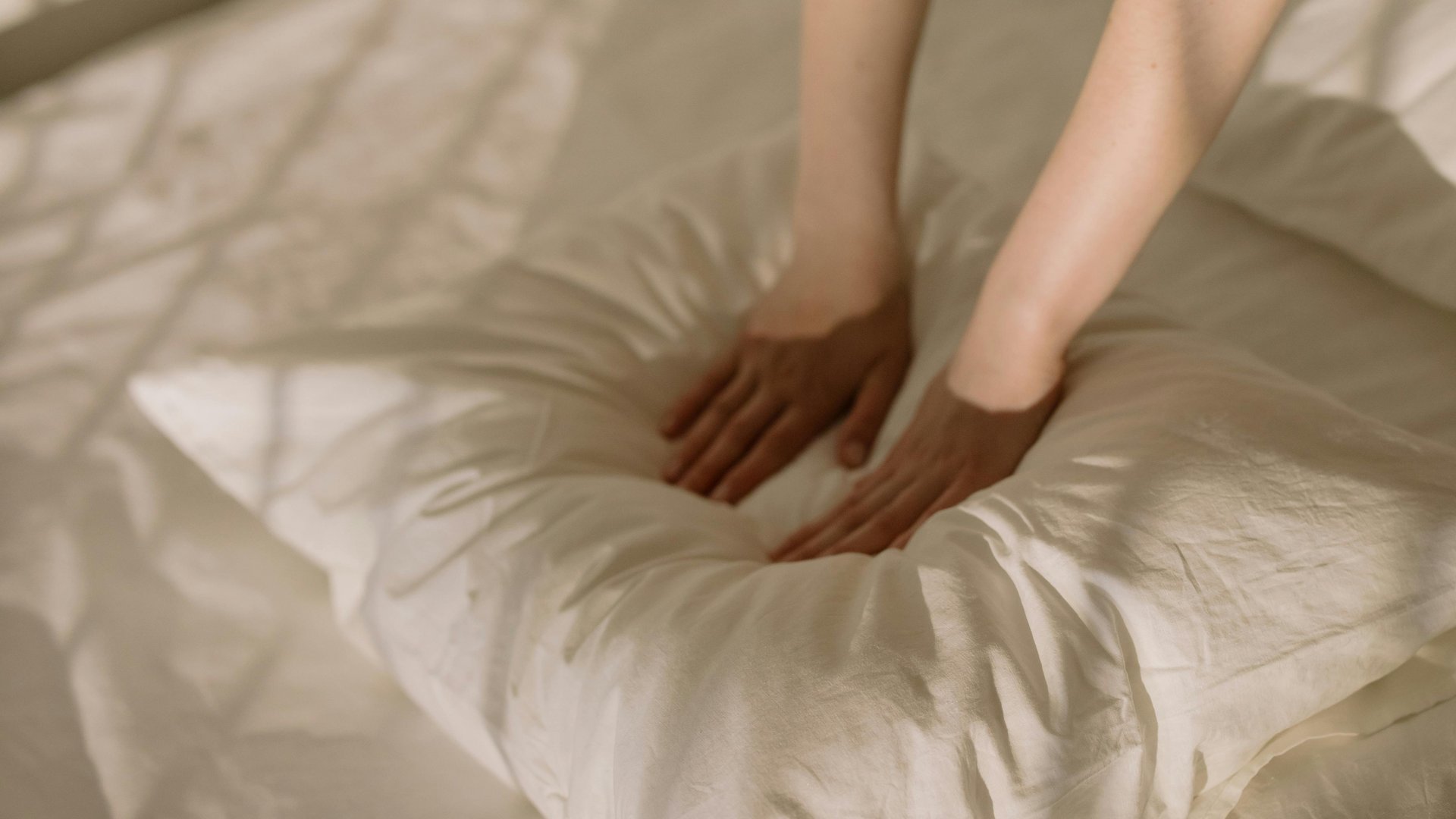 Mani che premono un cuscino bianco soffice su un letto